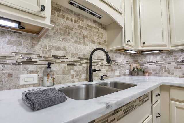 kitchen with backsplash, light stone counters, and sink