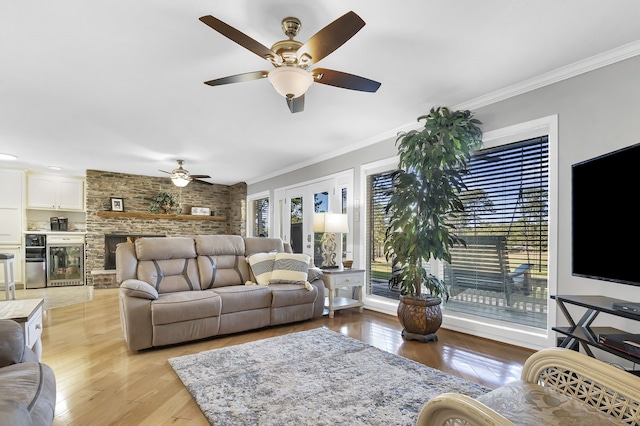 living room with ceiling fan, a stone fireplace, light wood-type flooring, and ornamental molding