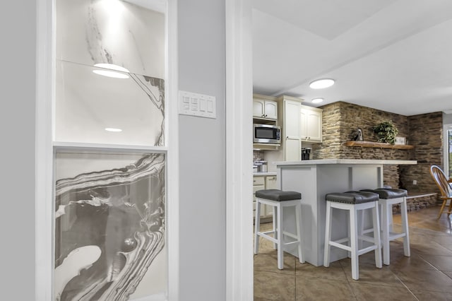 kitchen with a breakfast bar, kitchen peninsula, tile patterned floors, and stainless steel microwave