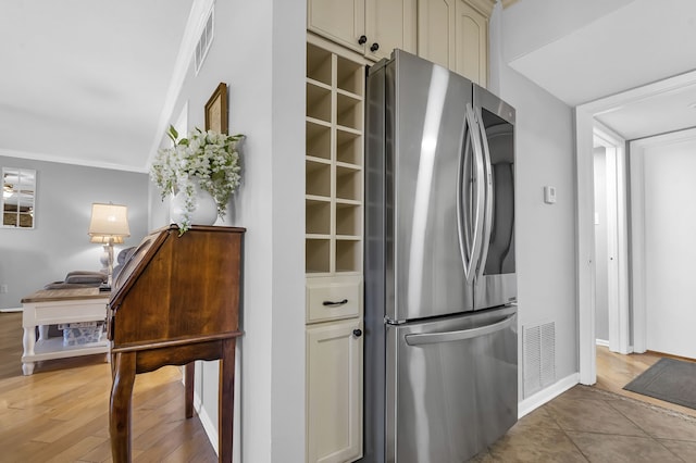 kitchen with cream cabinetry, light hardwood / wood-style floors, stainless steel refrigerator, and ornamental molding