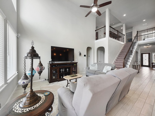 living room with a towering ceiling, ceiling fan, and light wood-type flooring