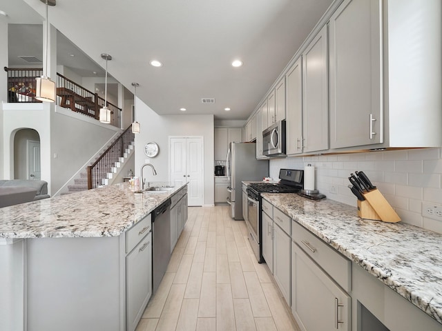 kitchen featuring pendant lighting, sink, appliances with stainless steel finishes, gray cabinetry, and light stone counters