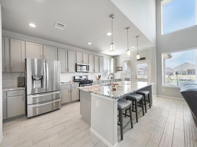 kitchen with sink, light stone counters, decorative light fixtures, appliances with stainless steel finishes, and an island with sink