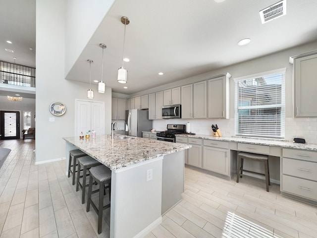 kitchen with gray cabinets, appliances with stainless steel finishes, pendant lighting, and a center island with sink