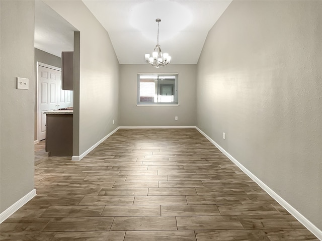 spare room featuring dark hardwood / wood-style floors, vaulted ceiling, and a notable chandelier