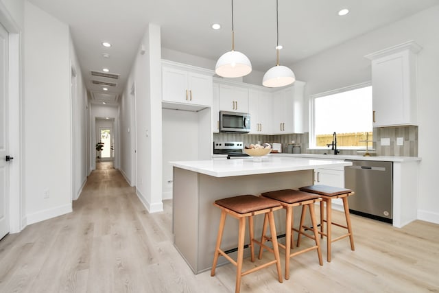 kitchen with white cabinetry, light hardwood / wood-style flooring, a kitchen island, and appliances with stainless steel finishes