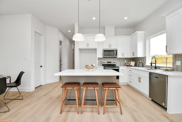 kitchen with white cabinetry, sink, stainless steel appliances, decorative light fixtures, and a kitchen island