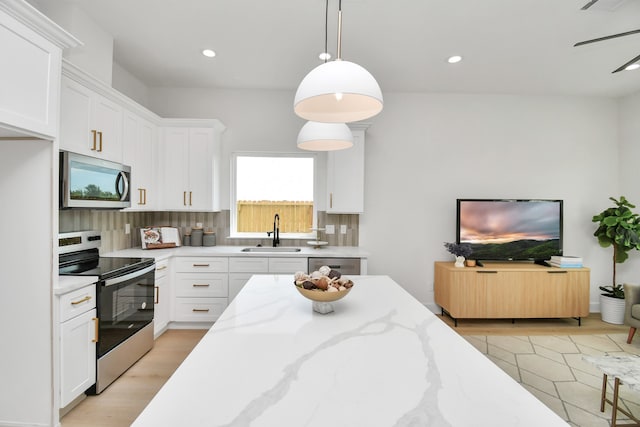 kitchen with pendant lighting, sink, light stone countertops, white cabinetry, and stainless steel appliances