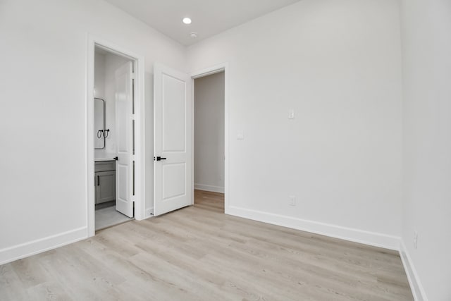 unfurnished bedroom with ensuite bathroom and light wood-type flooring