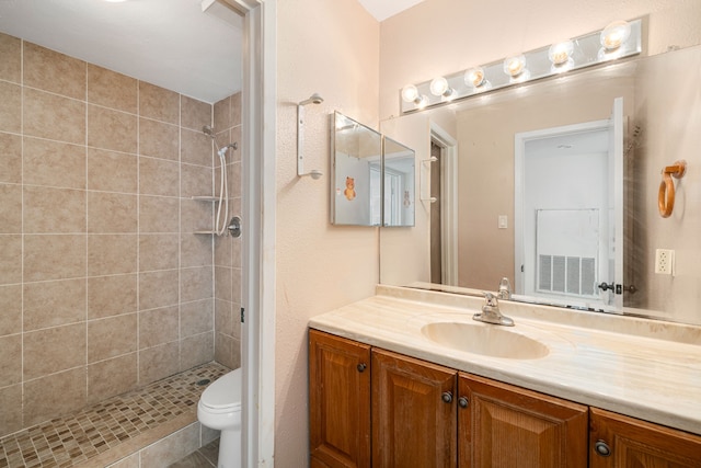 bathroom with a tile shower, vanity, and toilet