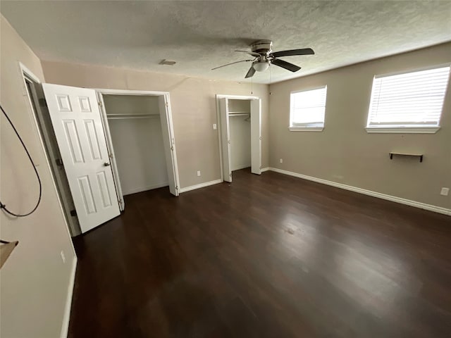 unfurnished bedroom with ceiling fan, dark hardwood / wood-style flooring, and two closets