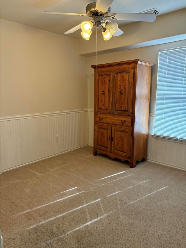 spare room featuring light colored carpet, a ceiling fan, and wainscoting