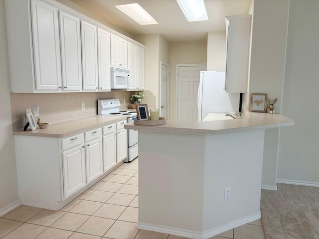 kitchen featuring a peninsula, white appliances, a skylight, white cabinets, and light countertops