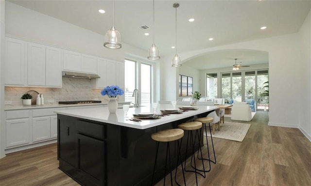 kitchen with ceiling fan, dark wood-type flooring, a large island with sink, decorative light fixtures, and white cabinets