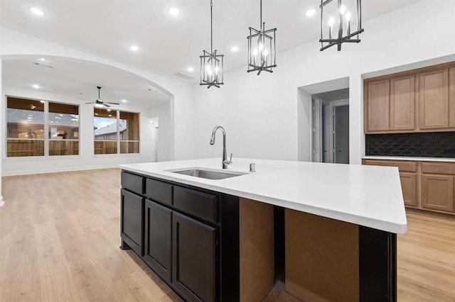 kitchen with decorative backsplash, a kitchen island with sink, sink, pendant lighting, and light hardwood / wood-style floors