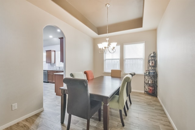 dining area with light hardwood / wood-style flooring, a tray ceiling, an inviting chandelier, and sink