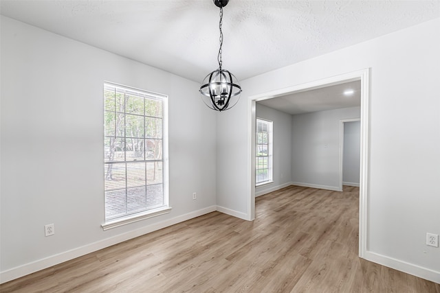 spare room featuring a textured ceiling, light hardwood / wood-style flooring, and a chandelier