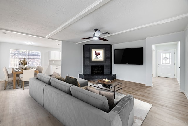 living room featuring a brick fireplace, a textured ceiling, ceiling fan, and light hardwood / wood-style floors