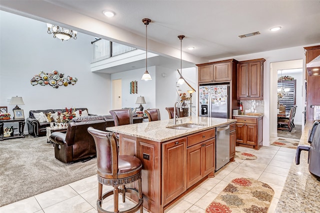 kitchen with light stone counters, hanging light fixtures, stainless steel appliances, a center island with sink, and sink