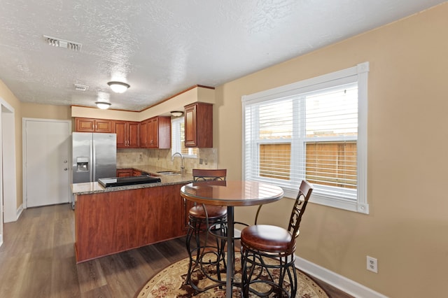 kitchen featuring sink, dark hardwood / wood-style flooring, stainless steel refrigerator with ice dispenser, kitchen peninsula, and a textured ceiling