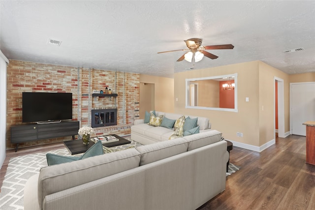 living room with ceiling fan with notable chandelier, a textured ceiling, dark hardwood / wood-style floors, and a brick fireplace