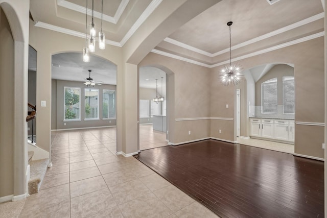 interior space with a tray ceiling, light hardwood / wood-style flooring, ceiling fan with notable chandelier, and ornamental molding