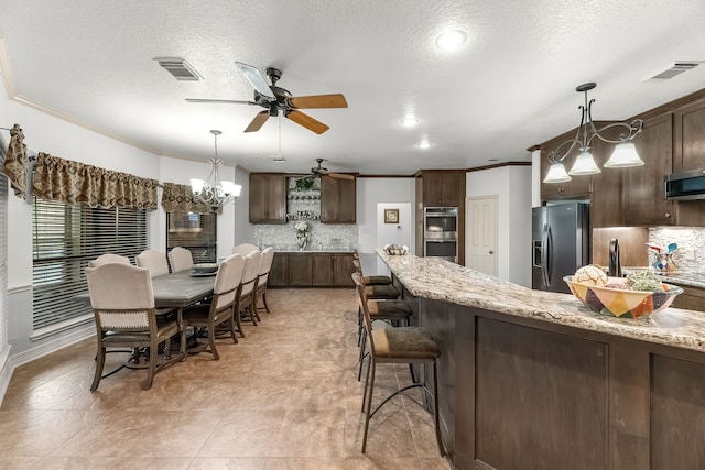 kitchen featuring decorative backsplash, appliances with stainless steel finishes, dark brown cabinetry, and light stone counters