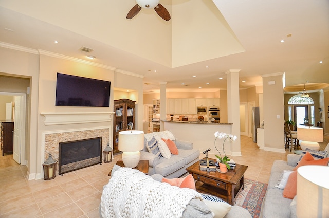 living room with ceiling fan, decorative columns, a fireplace, light tile patterned floors, and ornamental molding