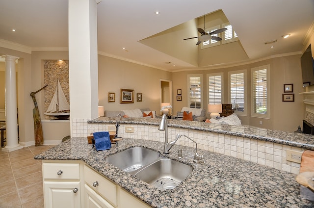 kitchen with ornamental molding, ceiling fan, sink, dark stone countertops, and a fireplace