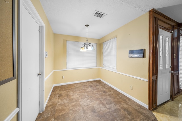 unfurnished dining area featuring a chandelier and a textured ceiling