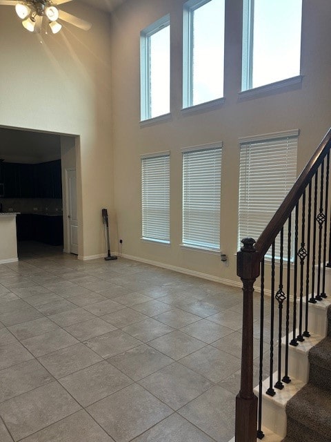 unfurnished living room featuring ceiling fan, light tile patterned floors, and a high ceiling