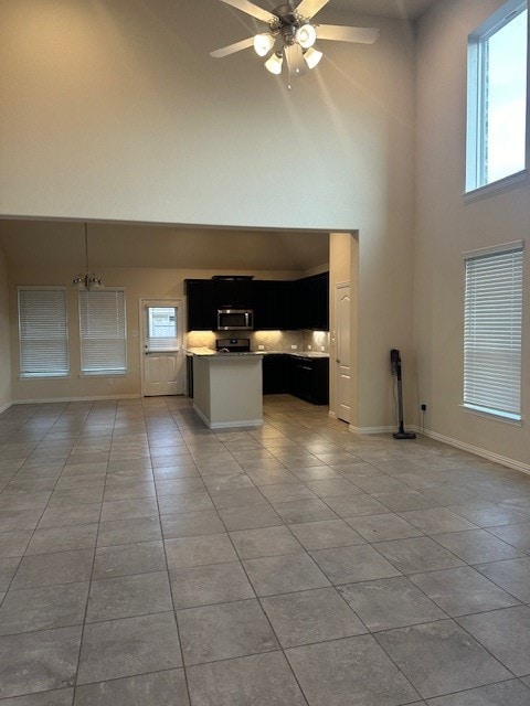 unfurnished living room with ceiling fan with notable chandelier, a towering ceiling, and light tile patterned flooring