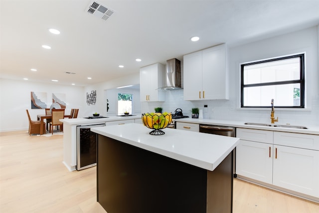 kitchen with a center island, sink, wall chimney exhaust hood, light hardwood / wood-style floors, and white cabinetry