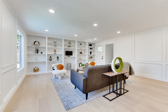 living room featuring built in shelves, light hardwood / wood-style floors, and crown molding