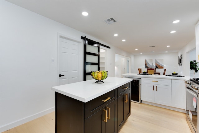 kitchen with stainless steel range with gas cooktop, wine cooler, a barn door, light wood-type flooring, and a kitchen island