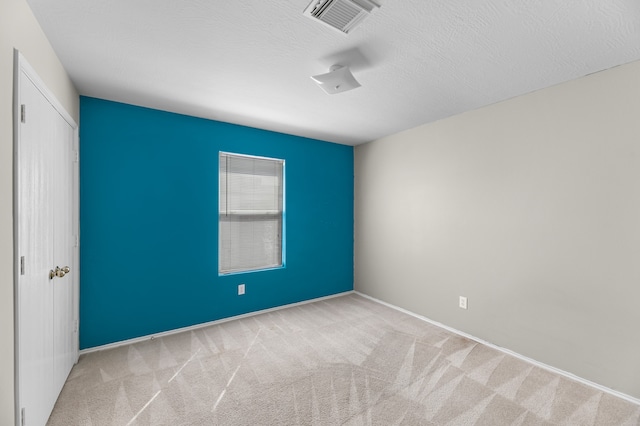 spare room featuring a textured ceiling and light colored carpet