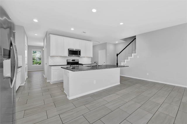 kitchen with a kitchen island with sink, white cabinets, sink, dark stone countertops, and appliances with stainless steel finishes