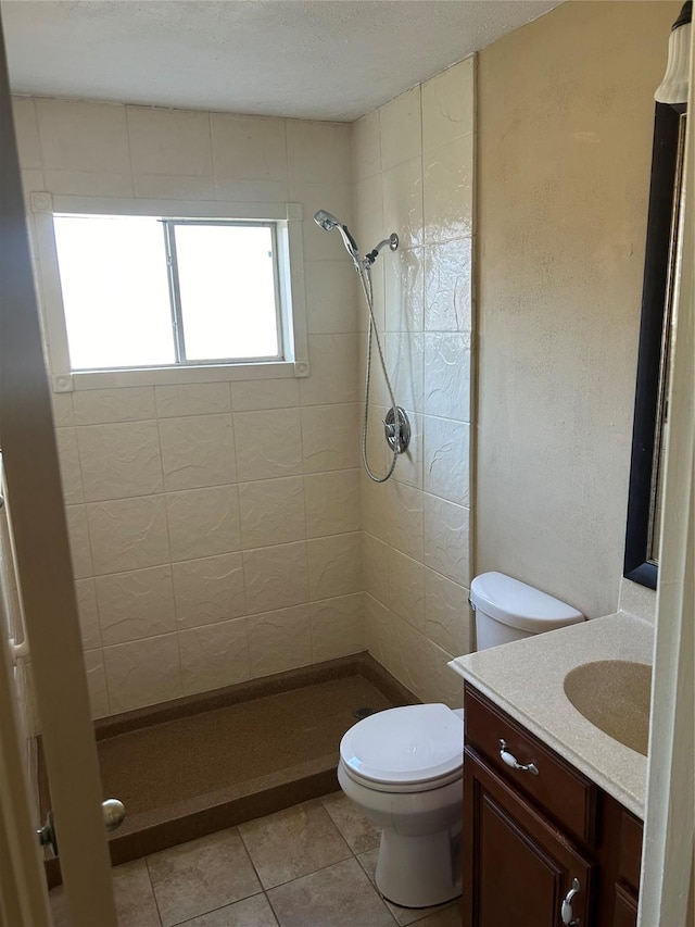 bathroom with tile patterned flooring, vanity, tiled shower, and toilet