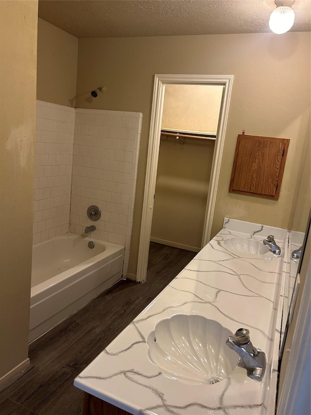 bathroom with wood-type flooring, vanity, a textured ceiling, and tiled shower / bath