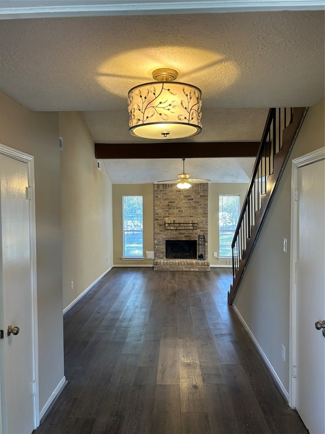 unfurnished living room featuring ceiling fan, dark hardwood / wood-style flooring, a textured ceiling, and a brick fireplace