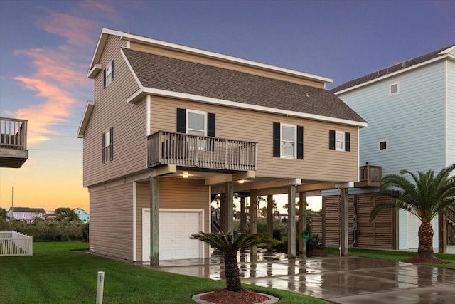 back house at dusk with a lawn, a balcony, a carport, and a garage