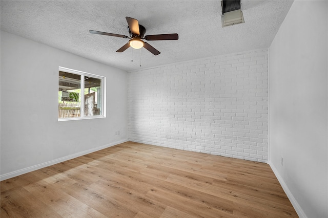 empty room featuring ceiling fan, light hardwood / wood-style floors, a textured ceiling, and brick wall