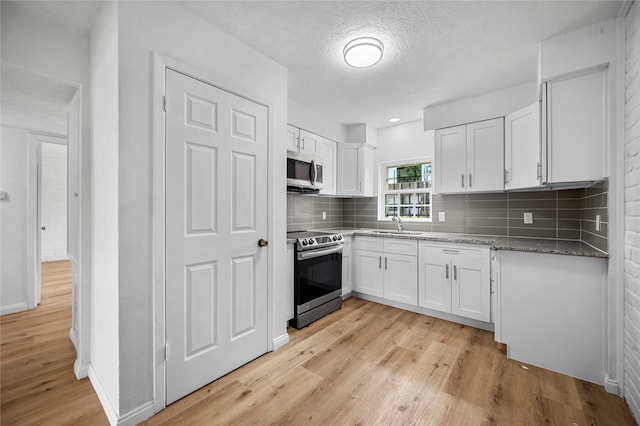 kitchen with stone counters, white cabinets, a textured ceiling, light hardwood / wood-style floors, and stainless steel appliances