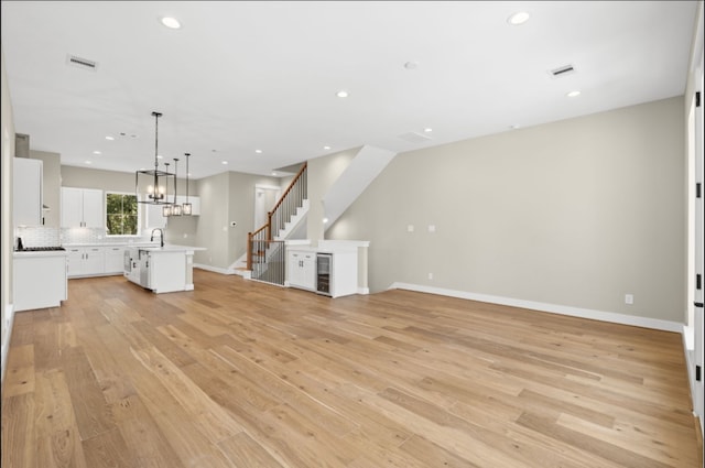 unfurnished living room with light hardwood / wood-style floors, sink, and wine cooler