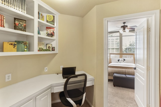 carpeted home office with ceiling fan and built in desk