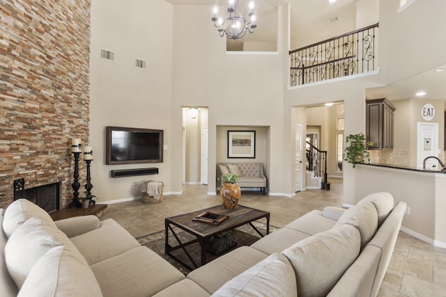 living room with a notable chandelier, a stone fireplace, a towering ceiling, and sink