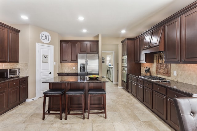 kitchen with dark brown cabinetry, stainless steel appliances, a kitchen breakfast bar, dark stone counters, and a kitchen island