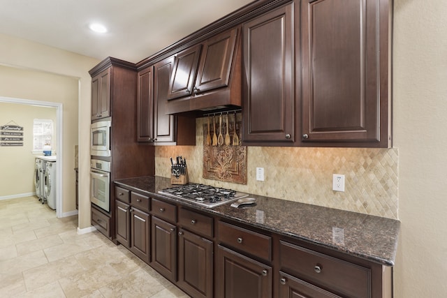 kitchen with washing machine and clothes dryer, dark brown cabinetry, backsplash, dark stone countertops, and appliances with stainless steel finishes