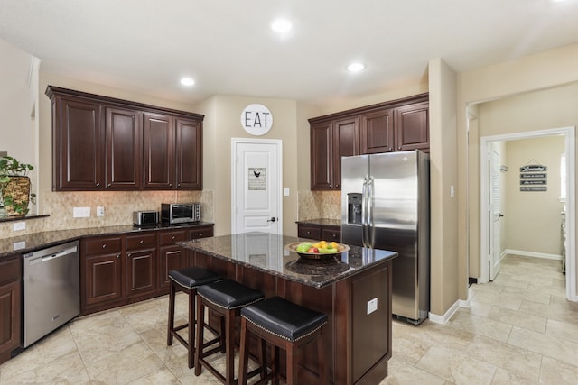 kitchen with backsplash, dark stone countertops, appliances with stainless steel finishes, dark brown cabinets, and a kitchen island