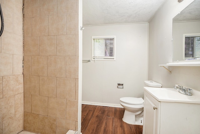 bathroom with vanity, a textured ceiling, tiled shower, hardwood / wood-style flooring, and toilet